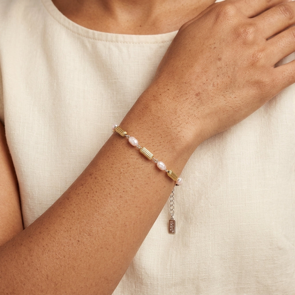Close up of a woman wearing our Faux Pearl Rice Bead & Cylindrical Gold Tone Bead Link Bracelet on her wrist. 
