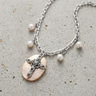 Faux Pearl Oval Disk Cross & Crystal Pendant Necklace resting on concrete surface