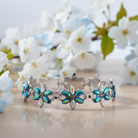 Silver bracelet with flower-shaped charms on a wooden surface with cherry blossoms in the background