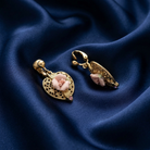 Gold earrings with pink floral elements on a blue fabric background