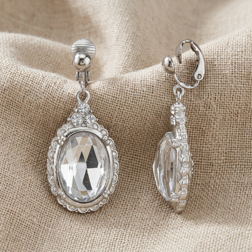 Silver tone earrings with clear crystals on a beige fabric background