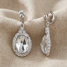 Silver tone earrings with clear crystals on a beige fabric background