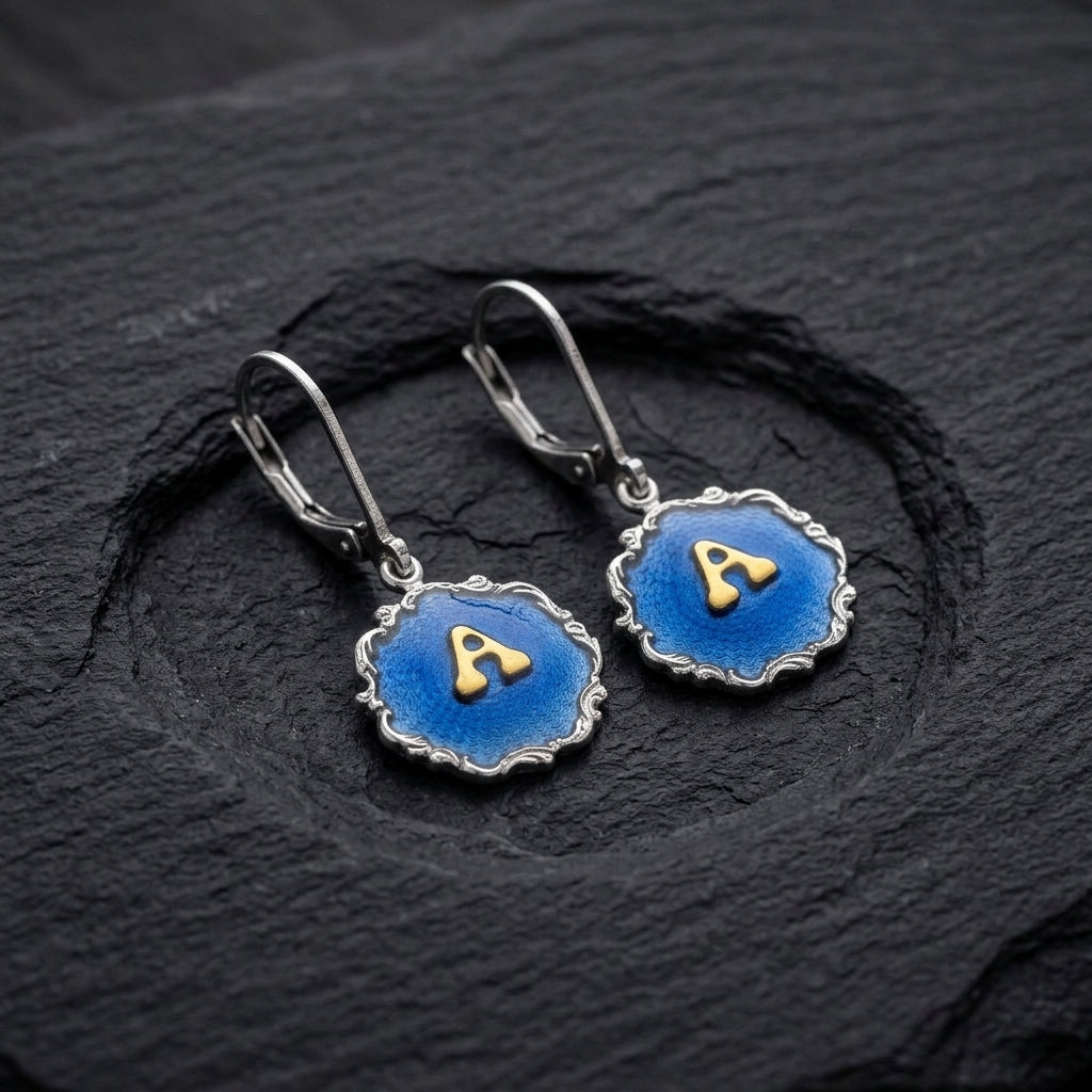 Sunburst Blue Enamel Initial Earrings resting on a black stone surface