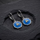 Sunburst Blue Enamel Initial Earrings resting on a black stone surface