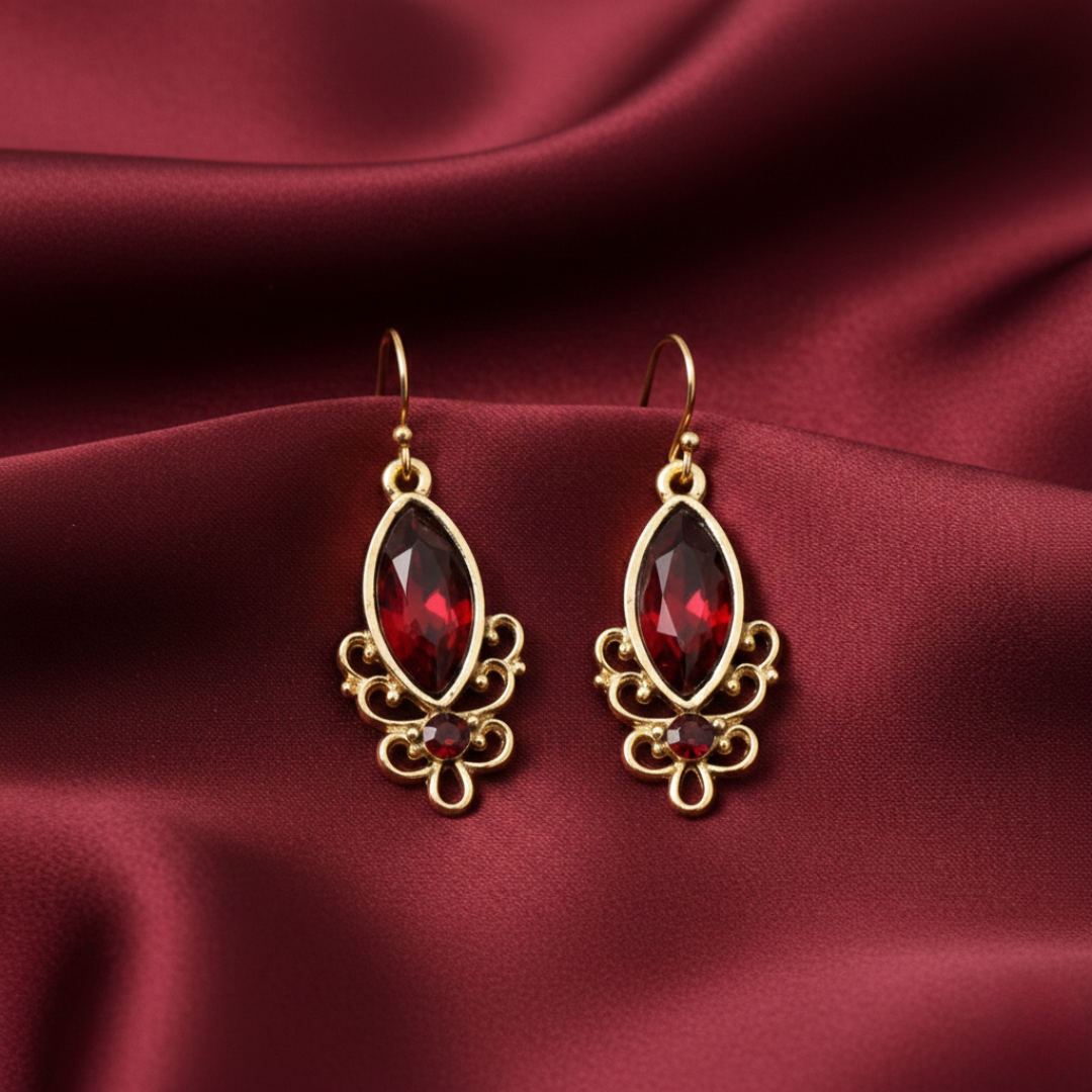 Gold earrings with red gemstones on a maroon fabric background