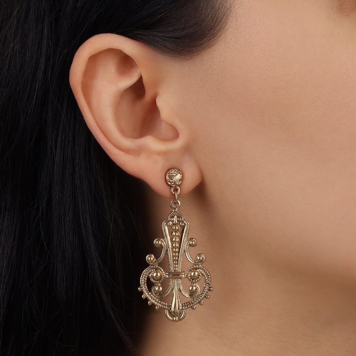 A close-up of a woman's ear wearing a Gold Tone Royal Filigree Ornamental Post Dangle Earrings