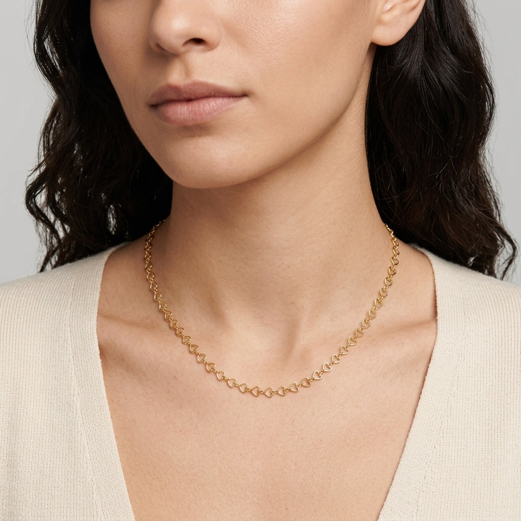 A close-up of a woman wearing a delicate gold chain necklace with small arrow-shaped links, paired with a cream-colored knit top.