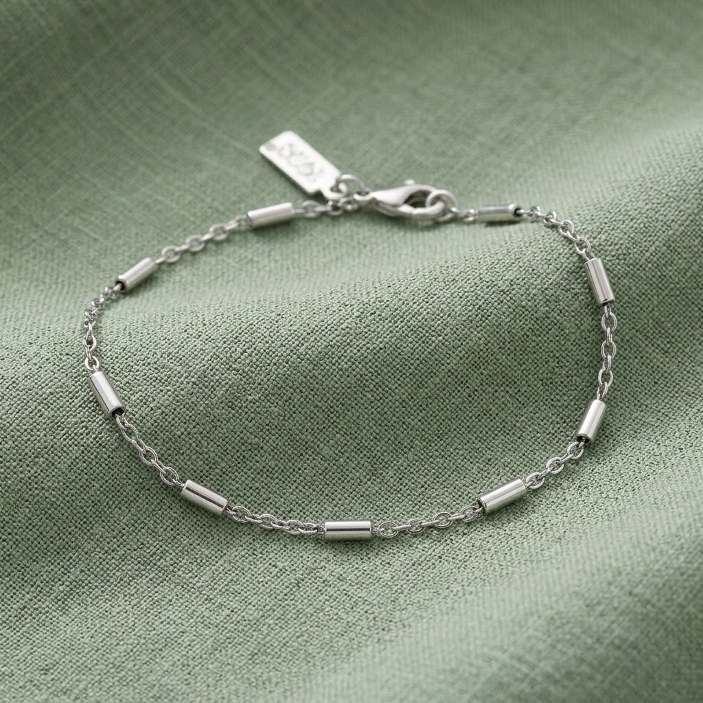 A silver chain bracelet with cable links and a lobster clasp, displayed on a textured sage green fabric background.