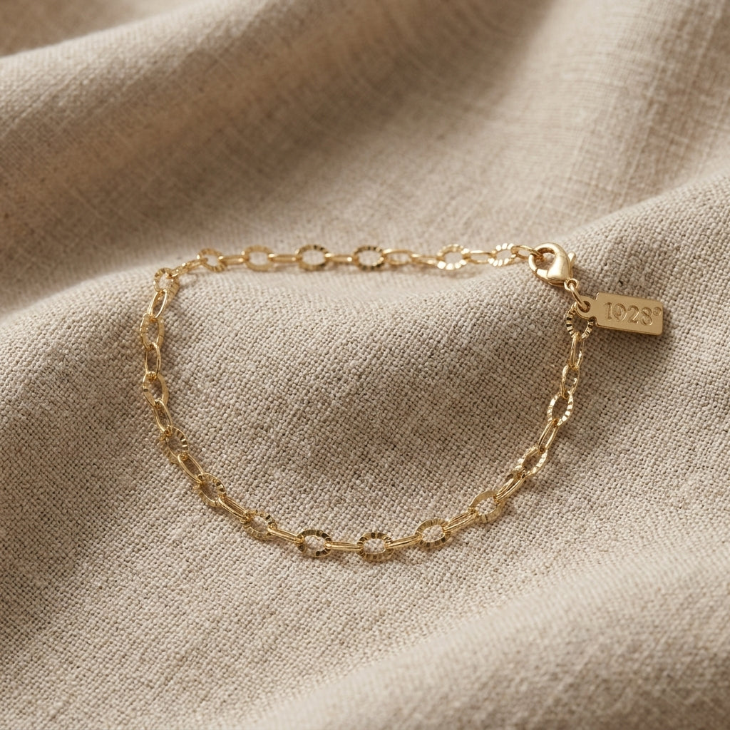 A delicate gold chain bracelet displayed on a textured beige linen fabric background.