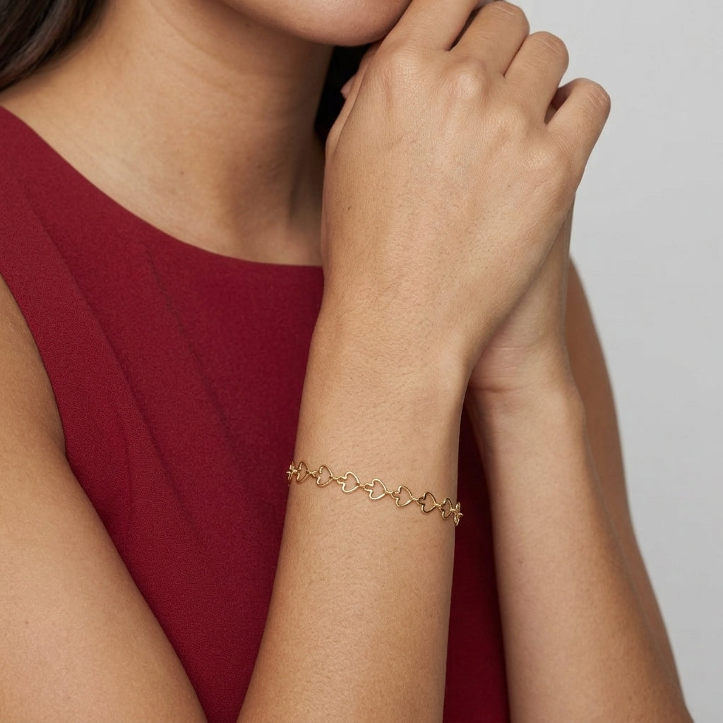 A delicate gold chain bracelet with small arrow-shaped links, worn on a woman's wrist. The model is wearing a dark red sleeveless top, and the background is a clean, neutral light gray.