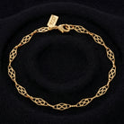 A gold link bracelet with an openwork geometric diamond pattern, displayed on a black textured background. 