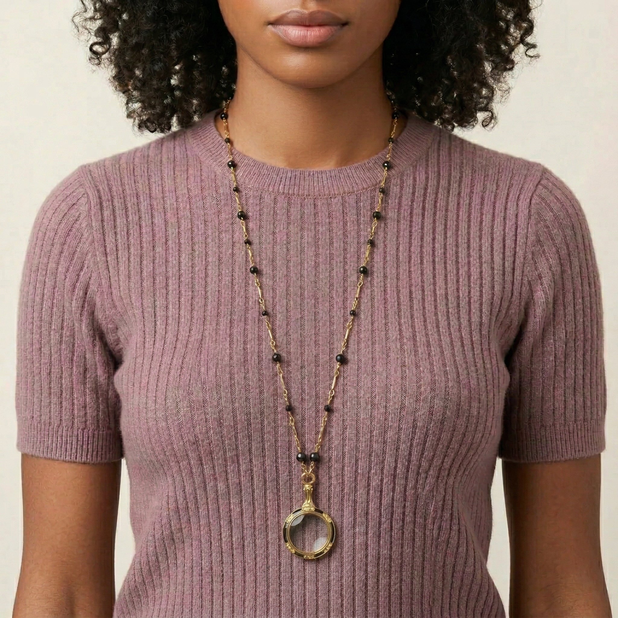 Woman wearing a gold necklace with black beads and a magnifying glass pendant