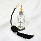 Decorative glass spray bottle with gold cap and black tassel on a white background