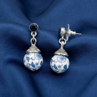 Pair of blue and white floral earrings on a blue fabric background