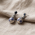 Blue Willow Round Beaded Post Drop Earrings resting on a beige linen fabric surface