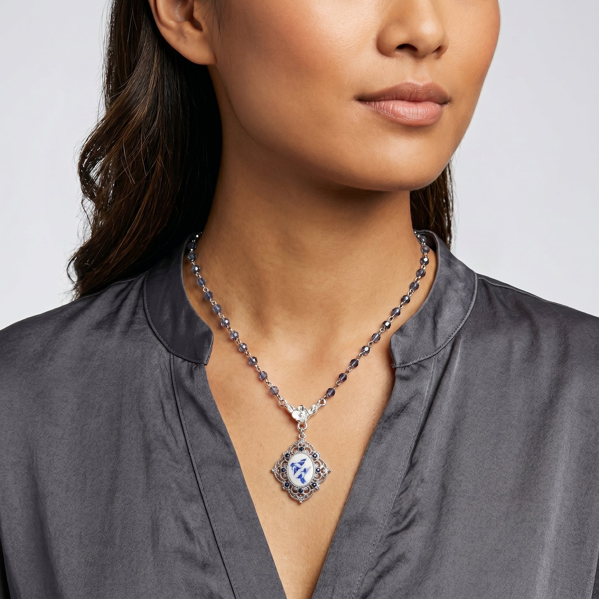 Blue beaded necklace with a Two Bird Blue Willow pendant and sapphire blue crystal accents worn by a woman with a dark top