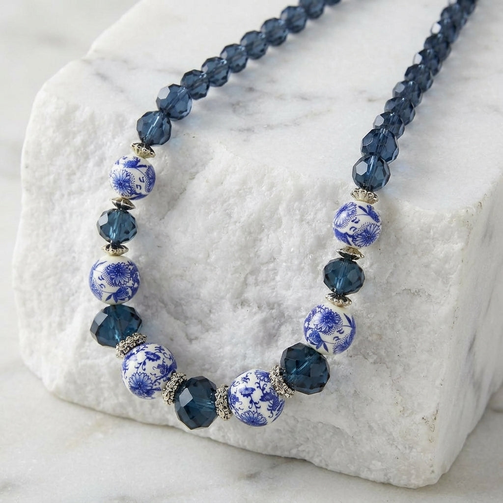Multi-shaped Montana Blue crystal beaded necklace with white floral decal beads resting atop white stone