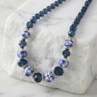Multi-shaped Montana Blue crystal beaded necklace with white floral decal beads resting atop white stone