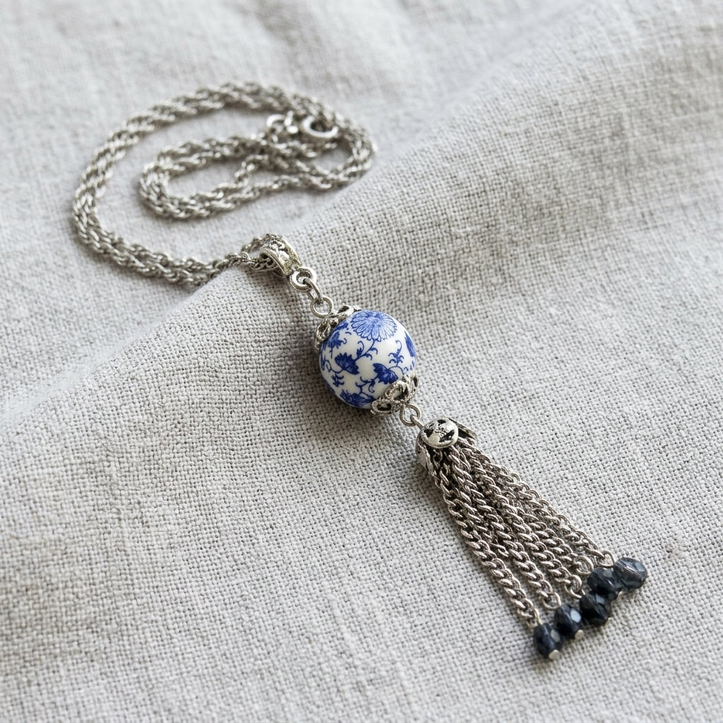 Necklace with a blue and white floral bead and silver tone tassel on a light fabric background