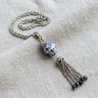 Necklace with a blue and white floral bead and silver tone tassel on a light fabric background