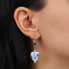 A close-up of a person's ear wearing a Blue Willow Blue Stone Heart Drop Earrings