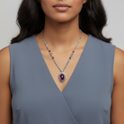 Woman wearing a gray sleeveless top with a necklace featuring a purple crystal and crystal beads on a silver chain.