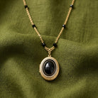 Necklace with a black stone locket pendant on a green fabric background