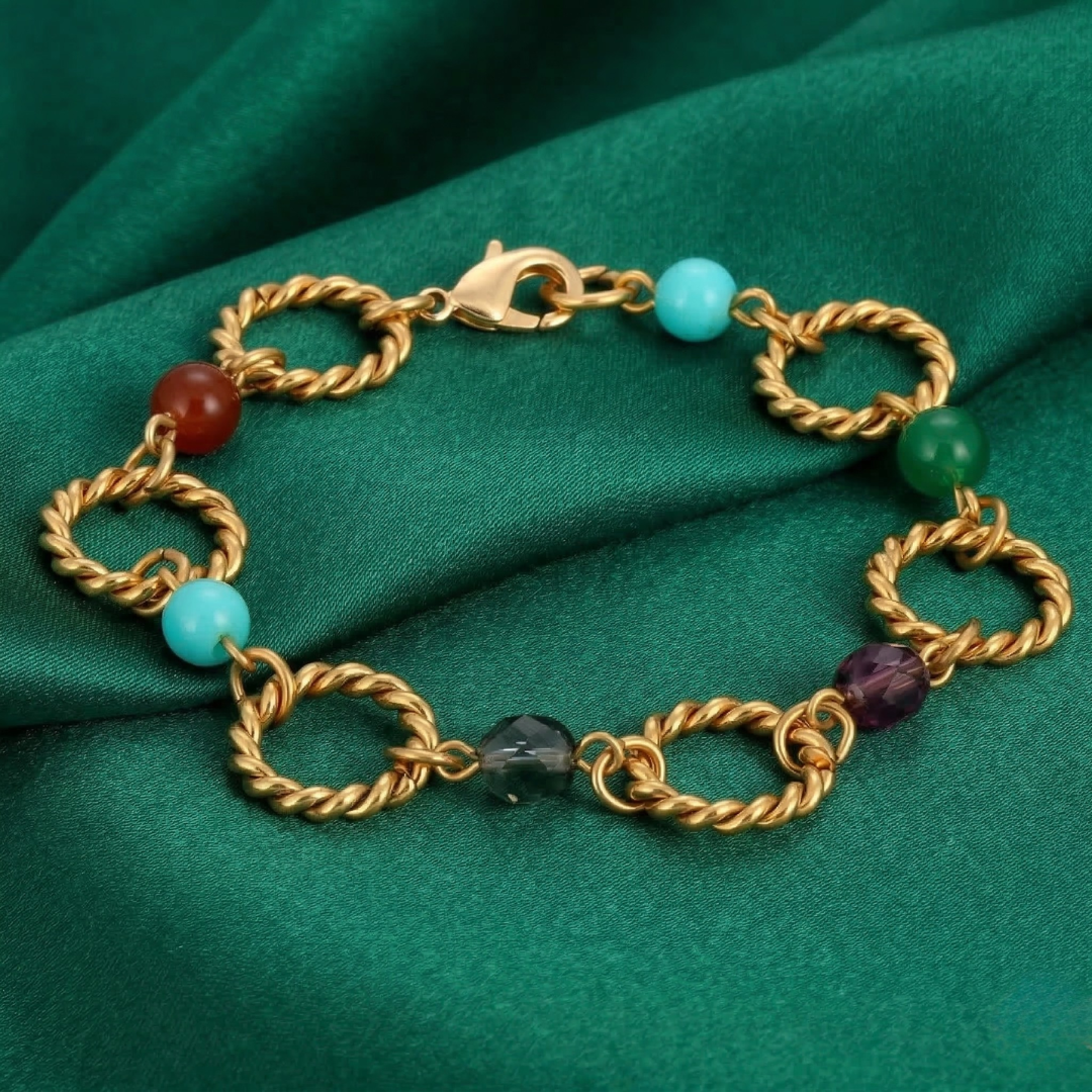 Gold chain bracelet with colored beads on a green fabric background