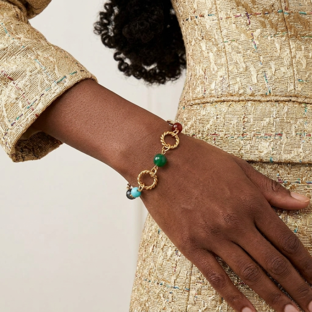 Close-up of a hand wearing a gold bracelet with multicolor beads, against a neutral background.