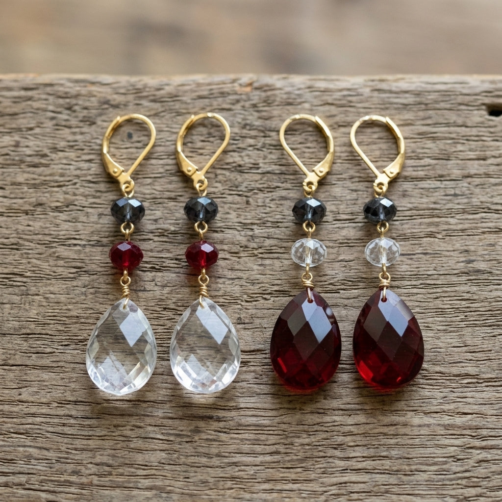 Two pairs of red, white and blue earrings with teardrop-shaped crystals on a wooden surface