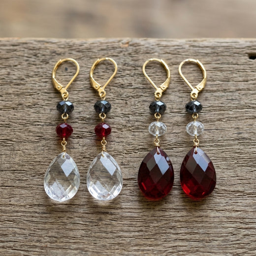 Two pairs of red, white and blue earrings with teardrop-shaped crystals on a wooden surface