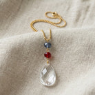 Necklace with a clear crystal pendant and colorful red and blue beads on a beige fabric background