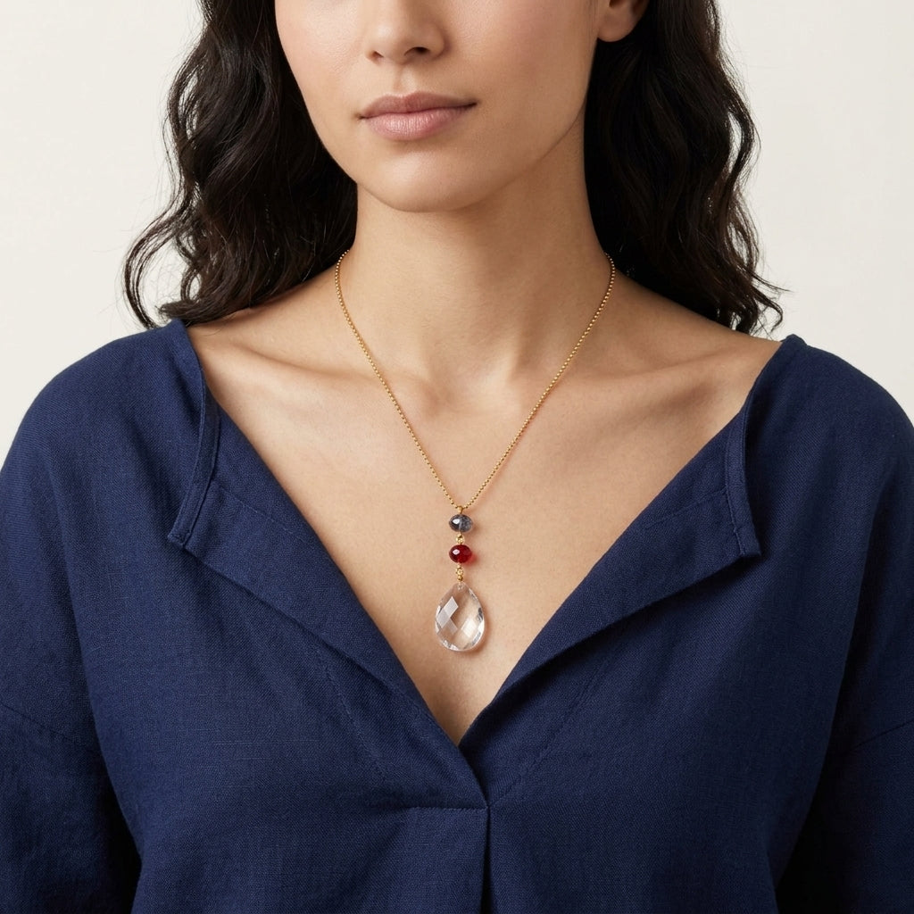 Woman wearing a necklace with a clear crystal pendant and red and blue beads against a neutral background