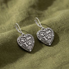 Heart Paws And Bones Drop Earrings resting on dark green linen