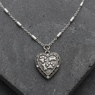 Silver tone Heart Paws And Bones Pendant Necklace resting on a dark stone surface
