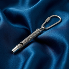 Silver whistle keychain with intricate design on a blue satin background