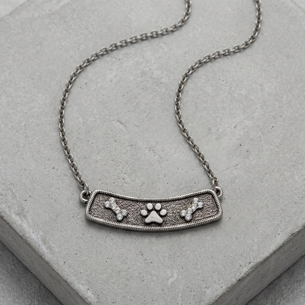 Crystal Bone And Paw Bar Pendant Necklace resting on a smooth concrete surface