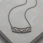 Crystal Bone And Paw Bar Pendant Necklace resting on a smooth concrete surface