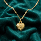 Petite puffed and etched gold tone heart pendant necklace resting on teal fabric