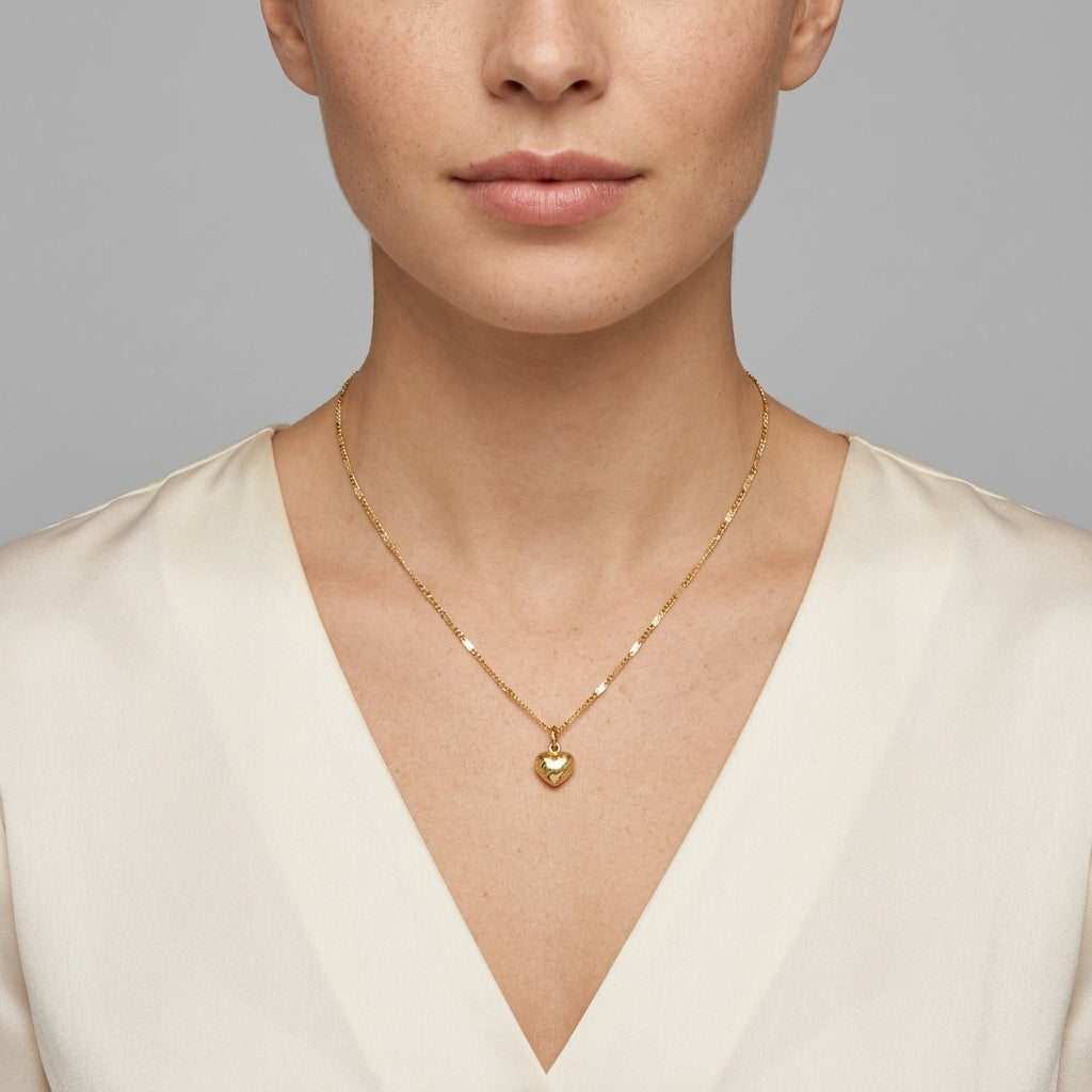 Woman in a white outfit wearing a petite puffed and etched gold tone heart pendant necklace