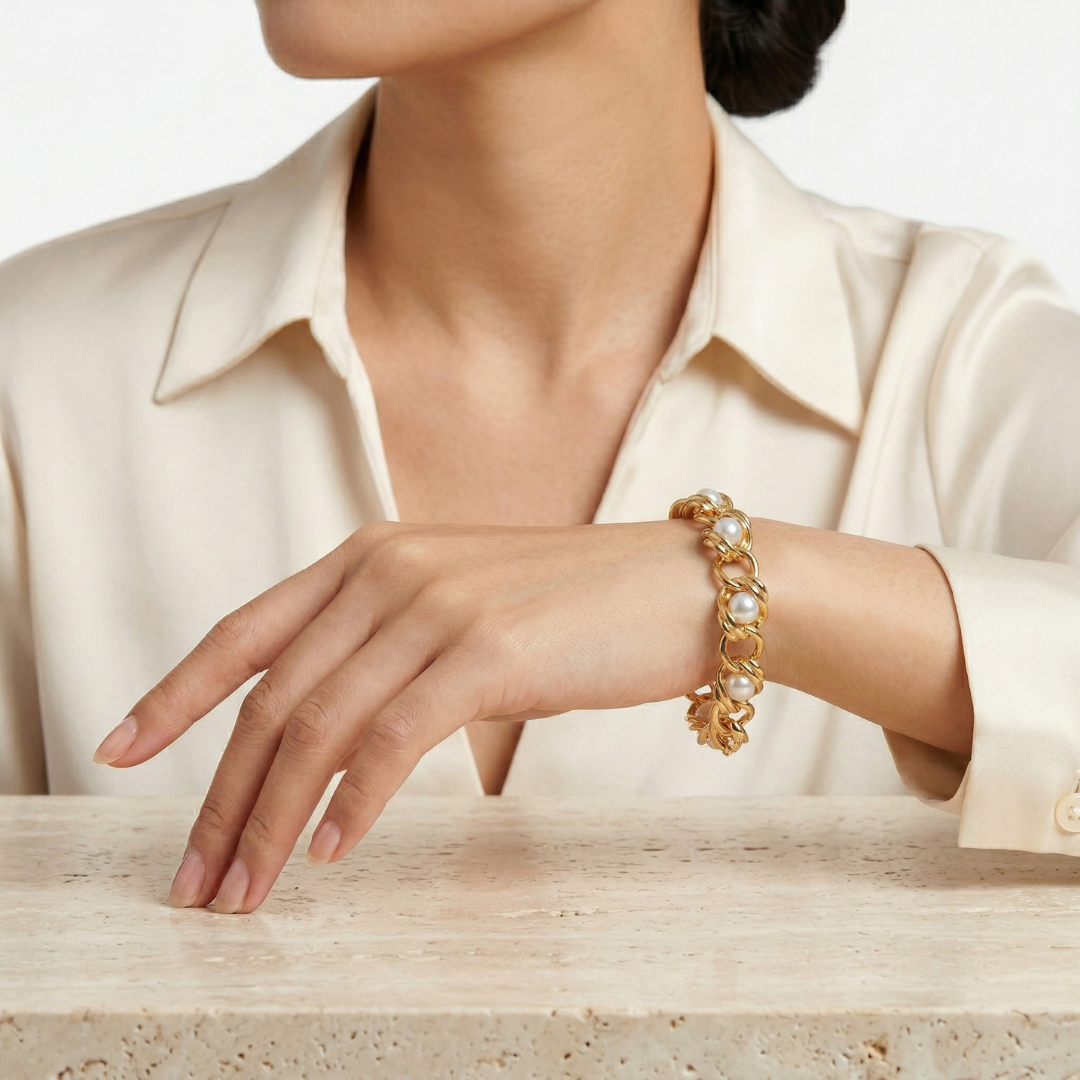 Woman in a white outfit wearing a gold tone chain bracelet with white faux pearls woven through