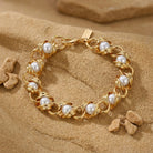 Gold tone chain bracelet with white faux pearls woven through resting on a sandstone surface