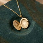 Gold tone Oval Flower & Faux Pearl Two Picture Locket Necklace opened and resting on a dark green stone surface
