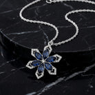 Sapphire blue crystal snowflake pendant necklace that has a silver tone chain resting on a black marble stone surface