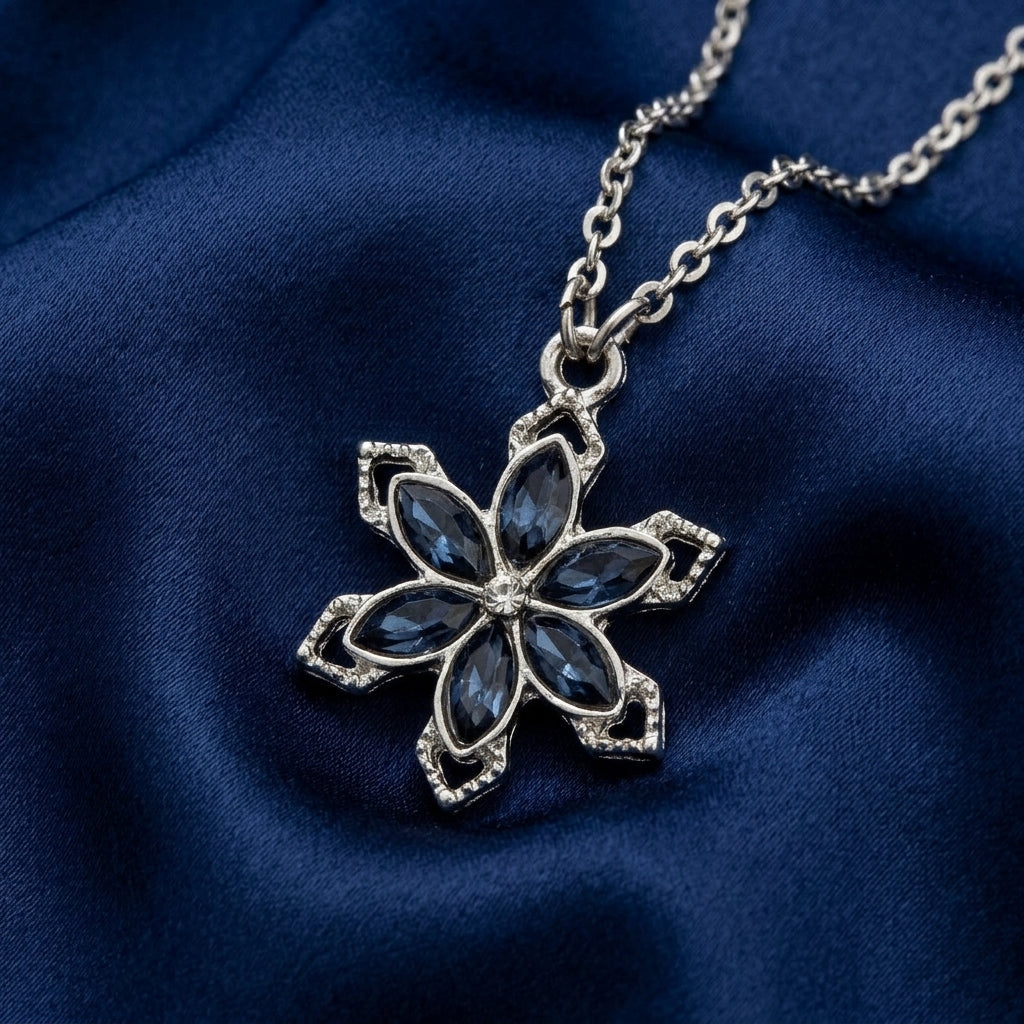 Sapphire blue crystal floral pendant necklace that has a silver tone chain resting on dark blue fabric