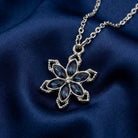 Sapphire blue crystal floral pendant necklace that has a silver tone chain resting on dark blue fabric