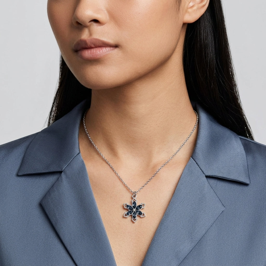 Woman in a silk top wearing a sapphire blue crystal floral pendant that has a silver tone chain
