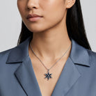 Woman in a silk top wearing a sapphire blue crystal floral pendant that has a silver tone chain