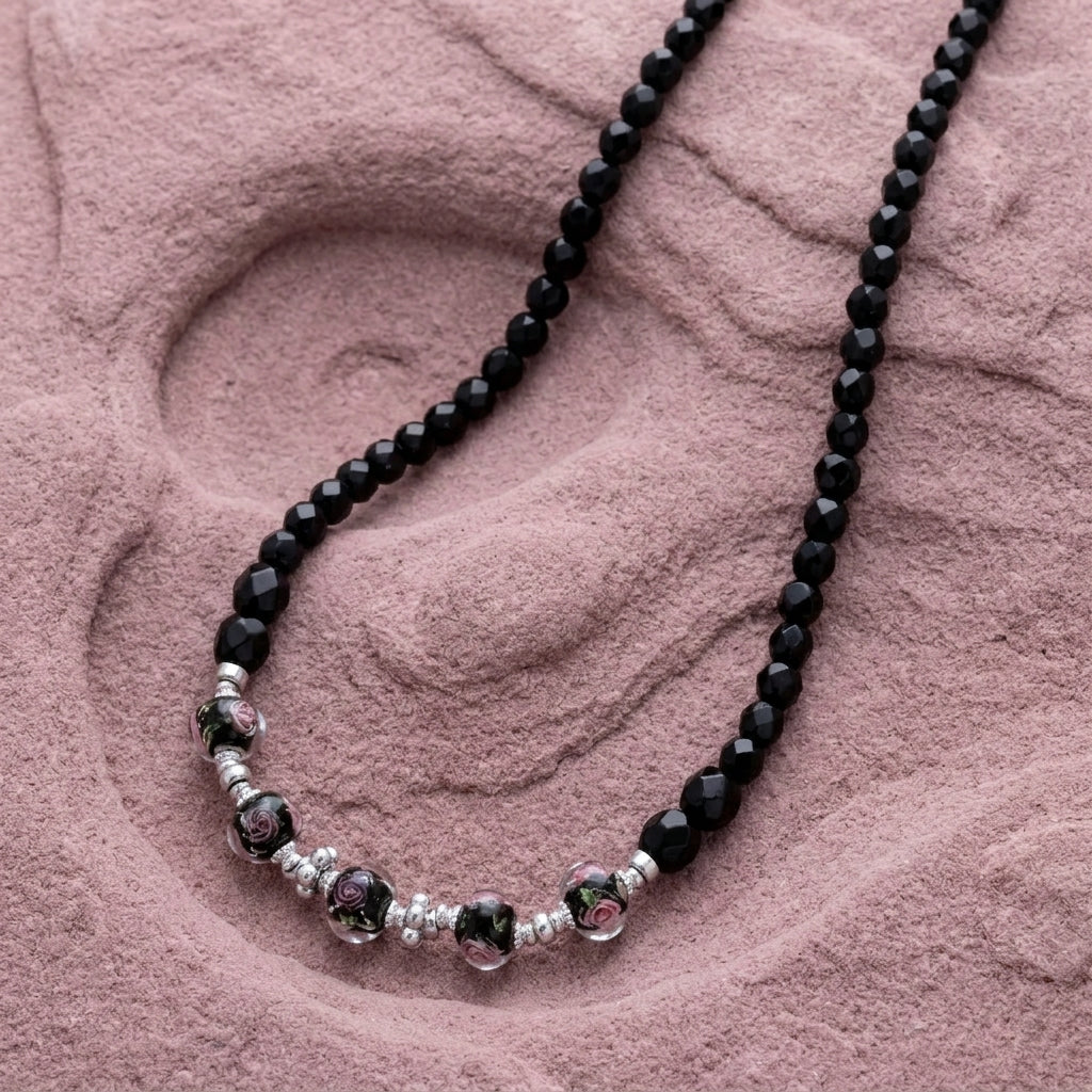 Black beaded necklace with pink floral motifs resting on a light purple stone surface
