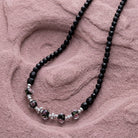 Black beaded necklace with pink floral motifs resting on a light purple stone surface